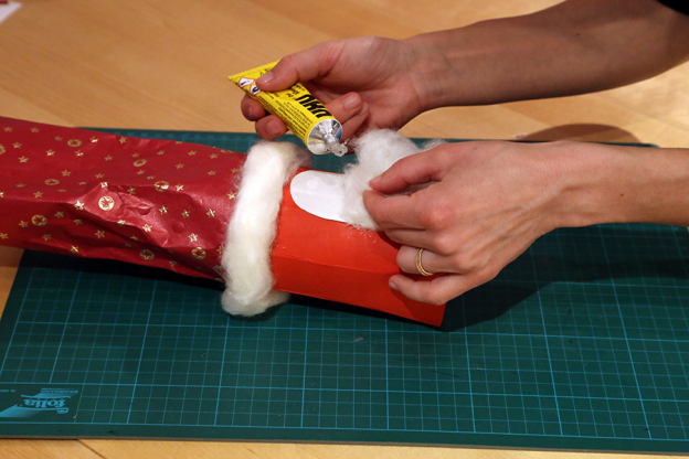 Mit Watte kannst du nun den Rand des Geschenkpapiers verzieren und das Gesicht des Nikolaus mit einem Bart und Haaren versehen.