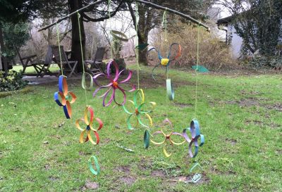 Mobile aus einer Holzstange mit Schnüren. An den Schnüren hängen bunte Blüten aus Papier.