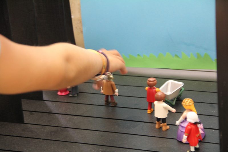Szene aus einem interaktiven Kinderworkshop im Domquartier Salzburg, zeigt eine Hand, die Figuren auf einem Trickfilmtisch arrangiert, um filmische Geschichten zu erzählen