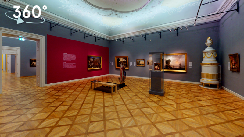 Ein barocker Raum mit Stuck an der Decke und einem kunstvollen Holzboden, barocke Bilder sind an den roten und grauen Wänden