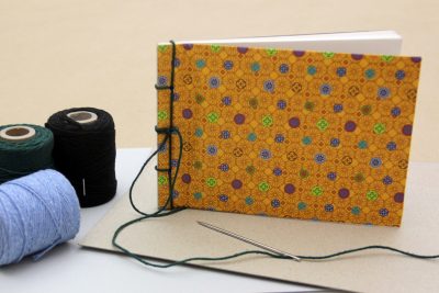 Handgemachtes Buch mit gelb gemustertem Stoffeinband und mit blauen Fäden gebunden