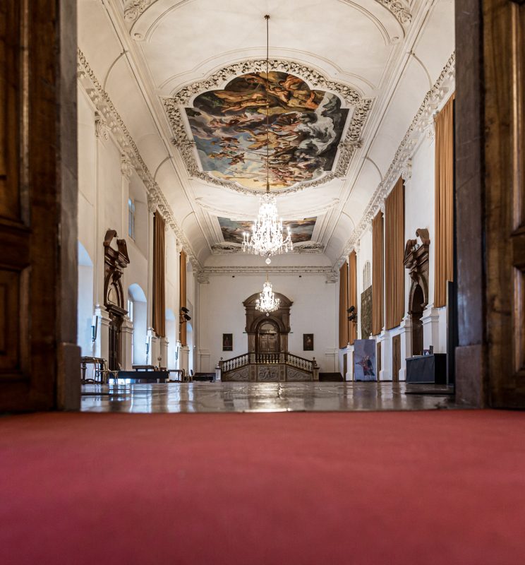 Ein prunkvoller Saal mit rotem Teppich und kunstvoll bemalter Decke im Domquartier